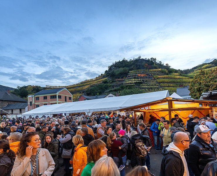 Menschenmenge auf dem Waagplatz in Mayschoß bei einer herbstlichen Veranstaltung mit Weinbergen im Hintergrund.