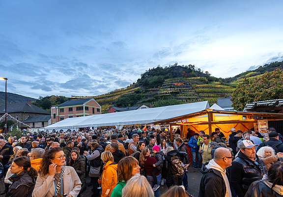 Menschenmenge auf dem Waagplatz in Mayschoß bei einer herbstlichen Veranstaltung mit Weinbergen im Hintergrund.