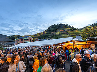 Menschenmenge auf dem Waagplatz in Mayschoß bei einer herbstlichen Veranstaltung mit Weinbergen im Hintergrund.